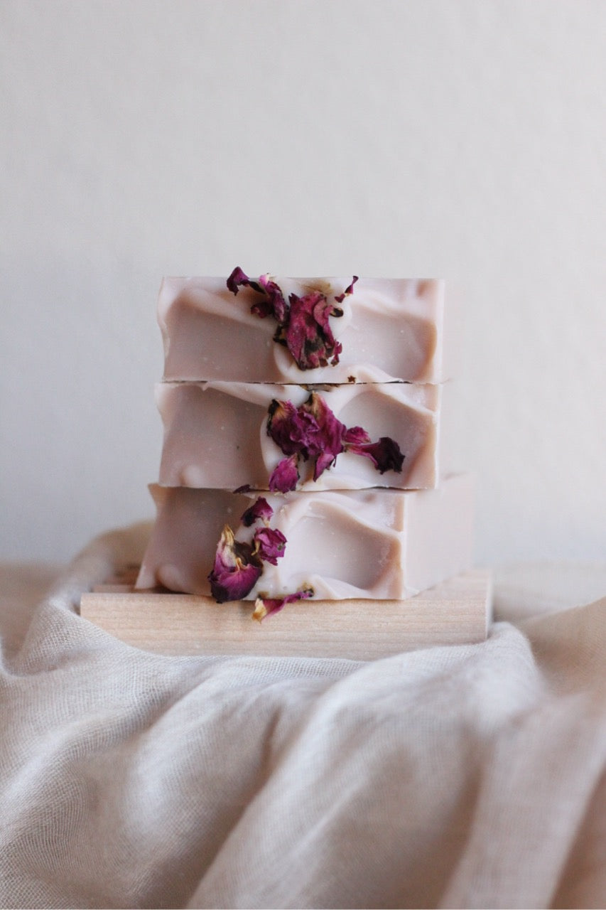Stack of pink soap bars with dried flowers on a wooden block against a neutral background