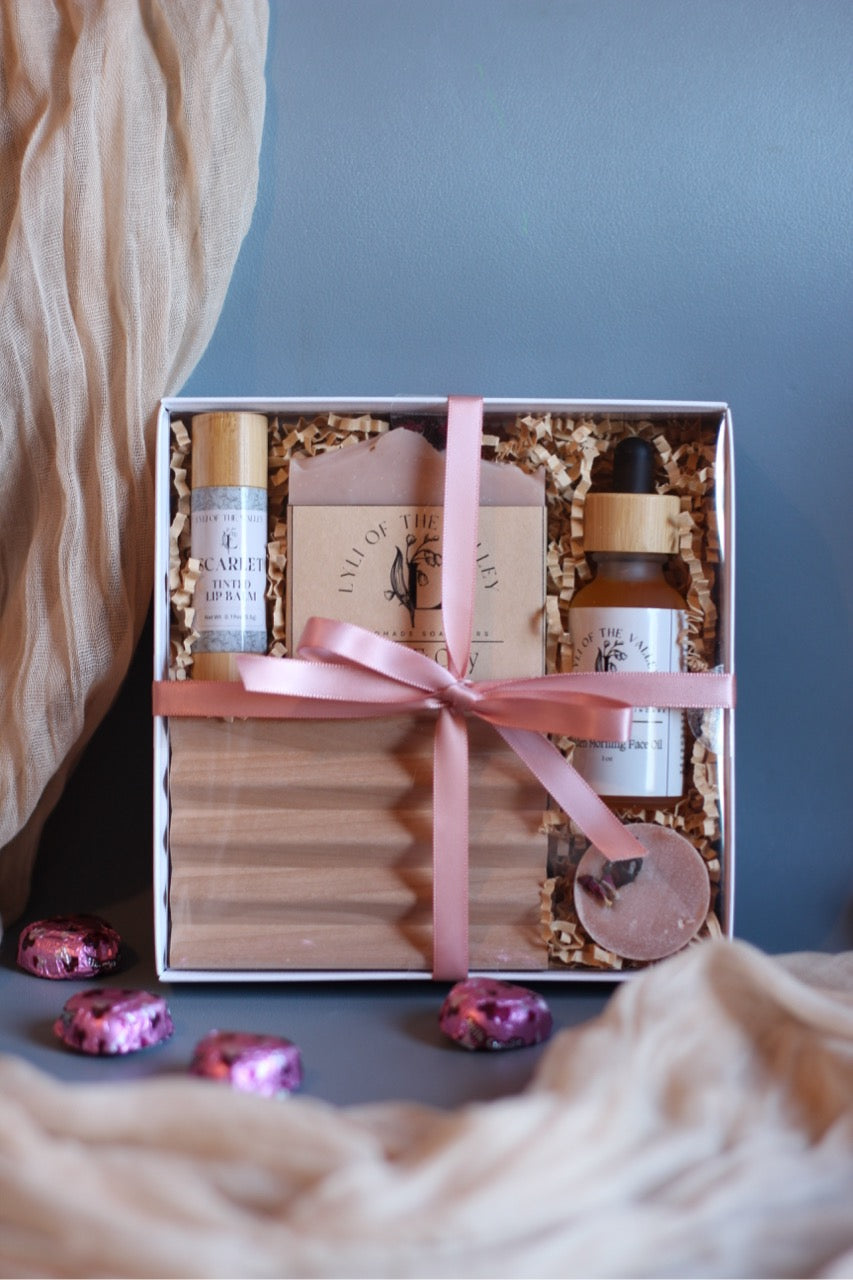 Gift set with skincare products in a box tied with a pink ribbon on a soft surface.