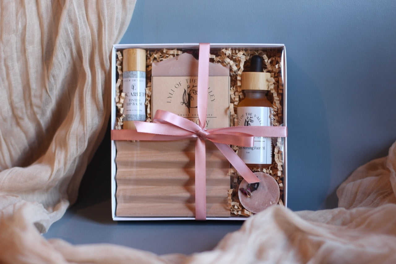 Gift set with skincare products in a box tied with a pink ribbon on a soft surface.